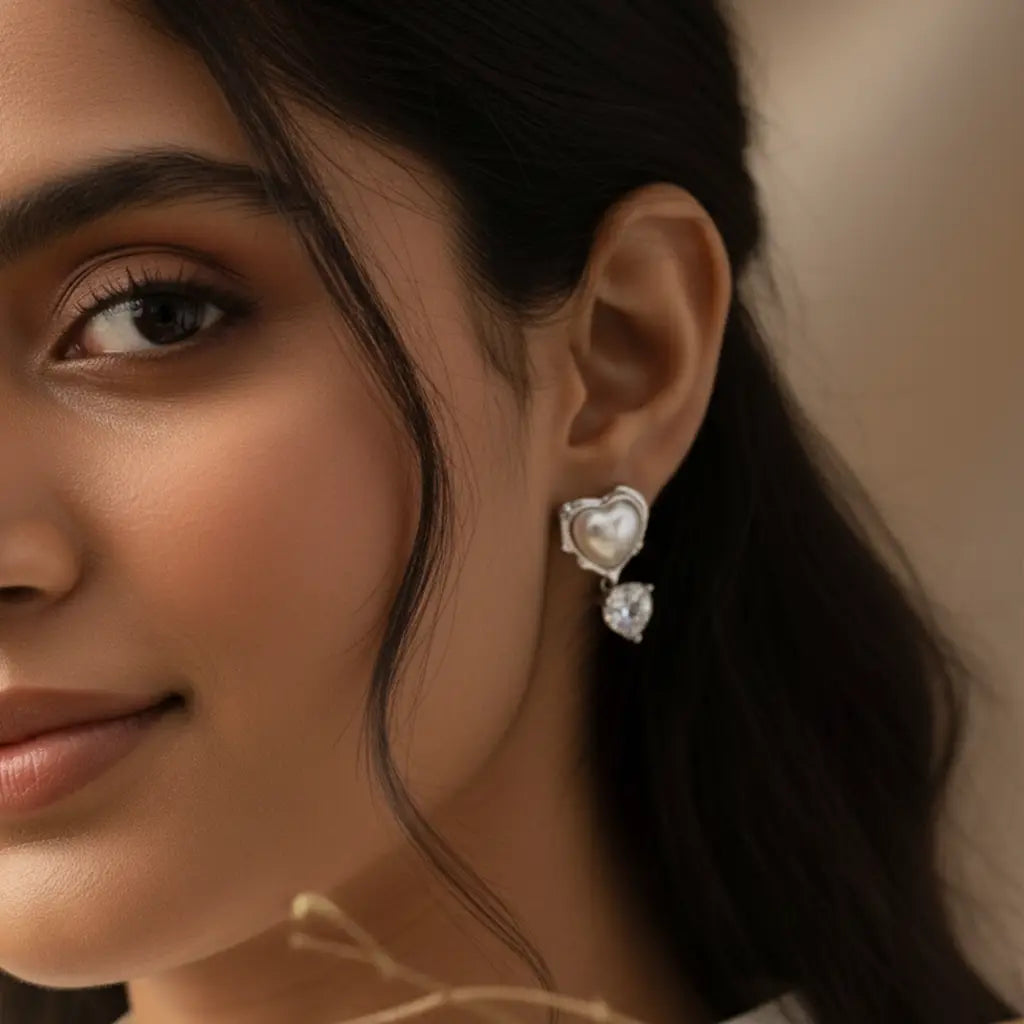 Close-up of a model wearing heart-shaped pearl and silver drop earrings with a sparkling cubic zirconia heart charm. Romantic and elegant fashion jewelry.