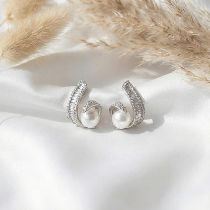 Anti tarnish silver swirl pearl earrings with cubic zirconia detailing on white satin background