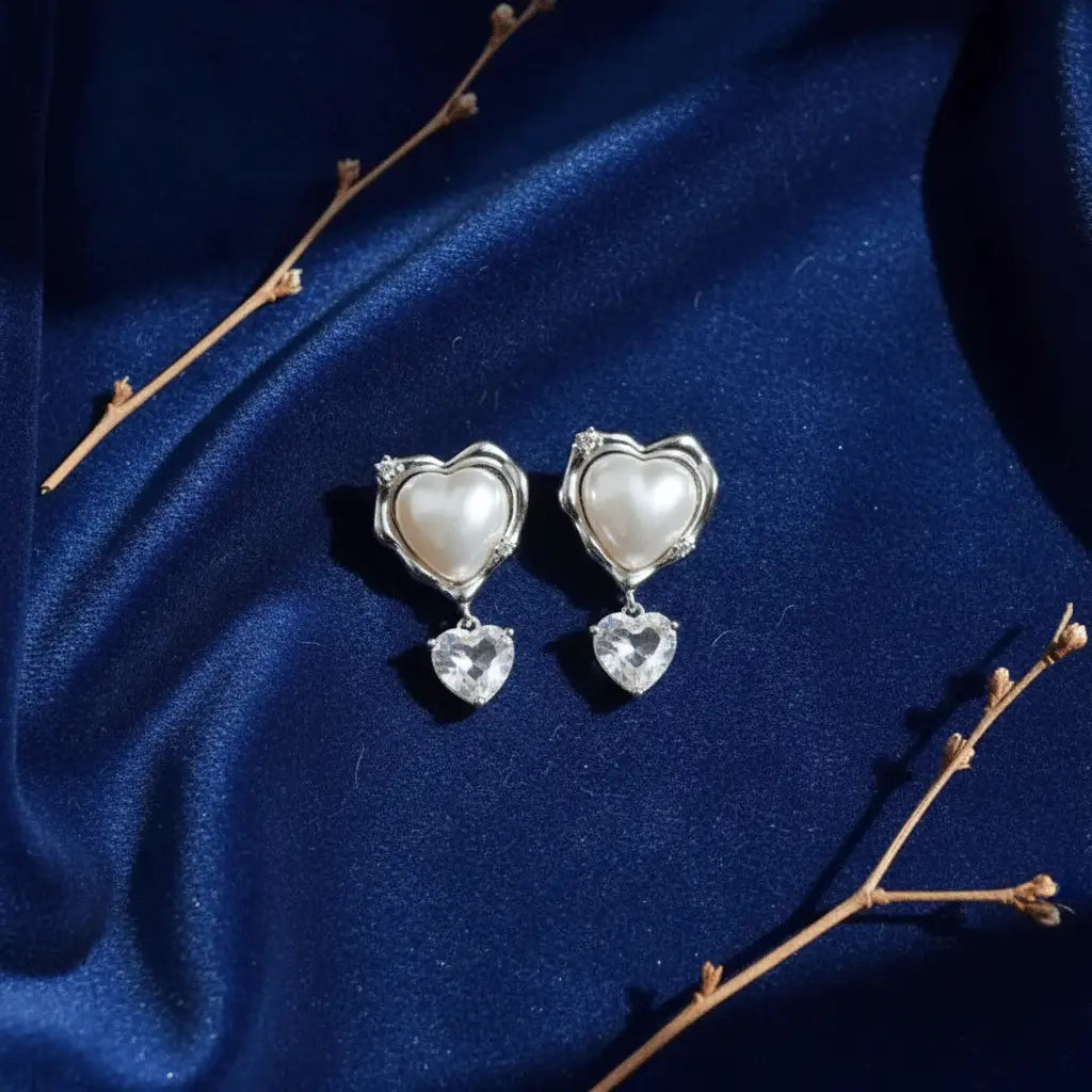 Sterling silver pearl heart drop earrings with dangling cubic zirconia heart accents on a rich navy blue silk background. Elegant bridal or gift jewelry.