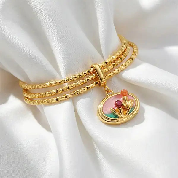 Pink Charm Bangle Bracelet with gold bangles and floral enamel charm on white satin cloth