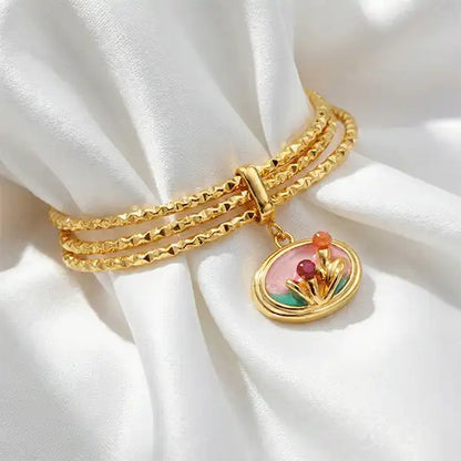 Pink Charm Bangle Bracelet with gold bangles and floral enamel charm on white satin cloth