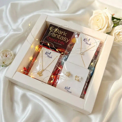 Queen of My Heart Valentine hamper featuring anti-tarnish gold-tone jewellery set with pendant necklace and earrings, Dark Fantasy Choco Fills, kitkat and fairy lights in a white gift box on satin fabric.