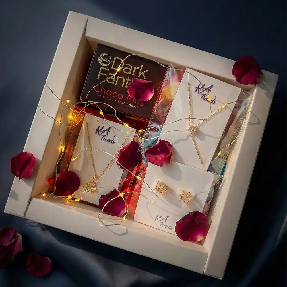 Romantic Valentine gift hamper with anti-tarnish jewellery set, Dark Fantasy chocolates, glowing fairy lights, and rose petals, presented in a premium white box on a dark background.