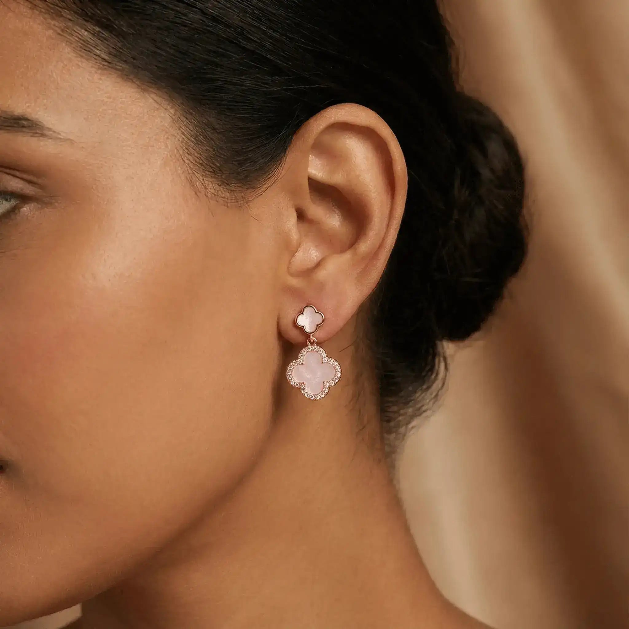 Rose gold clover drop earrings worn on ear with soft natural lighting