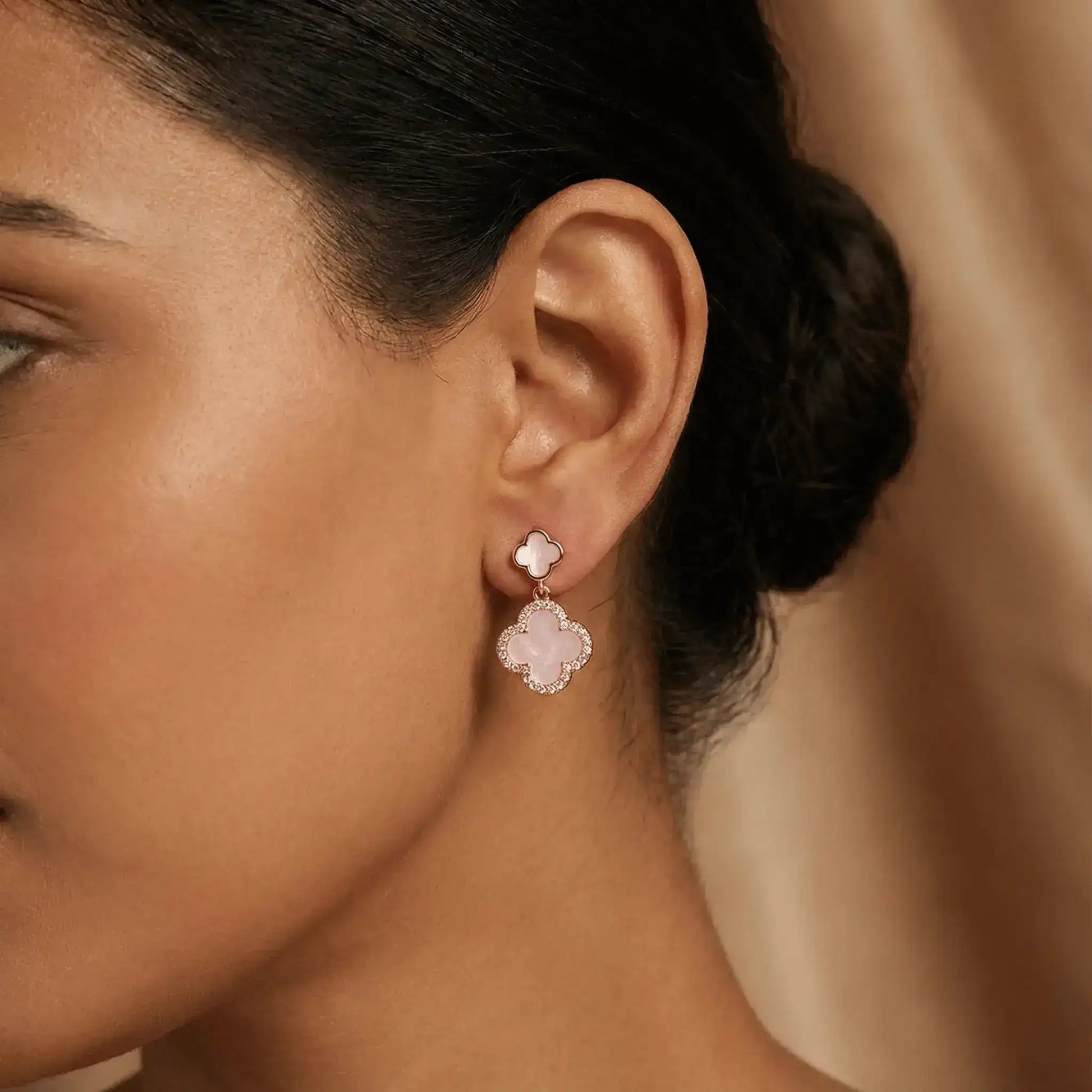 Rose gold clover drop earrings worn on ear with soft natural lighting
