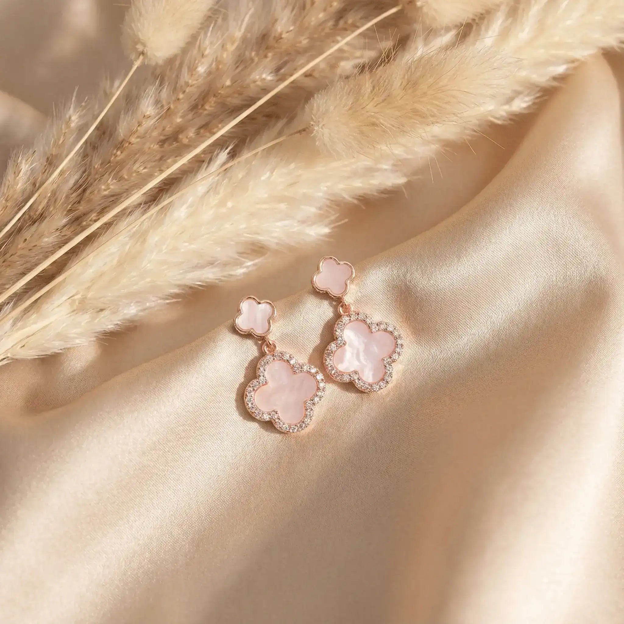 Rose gold clover drop earrings on beige satin with pampas grass