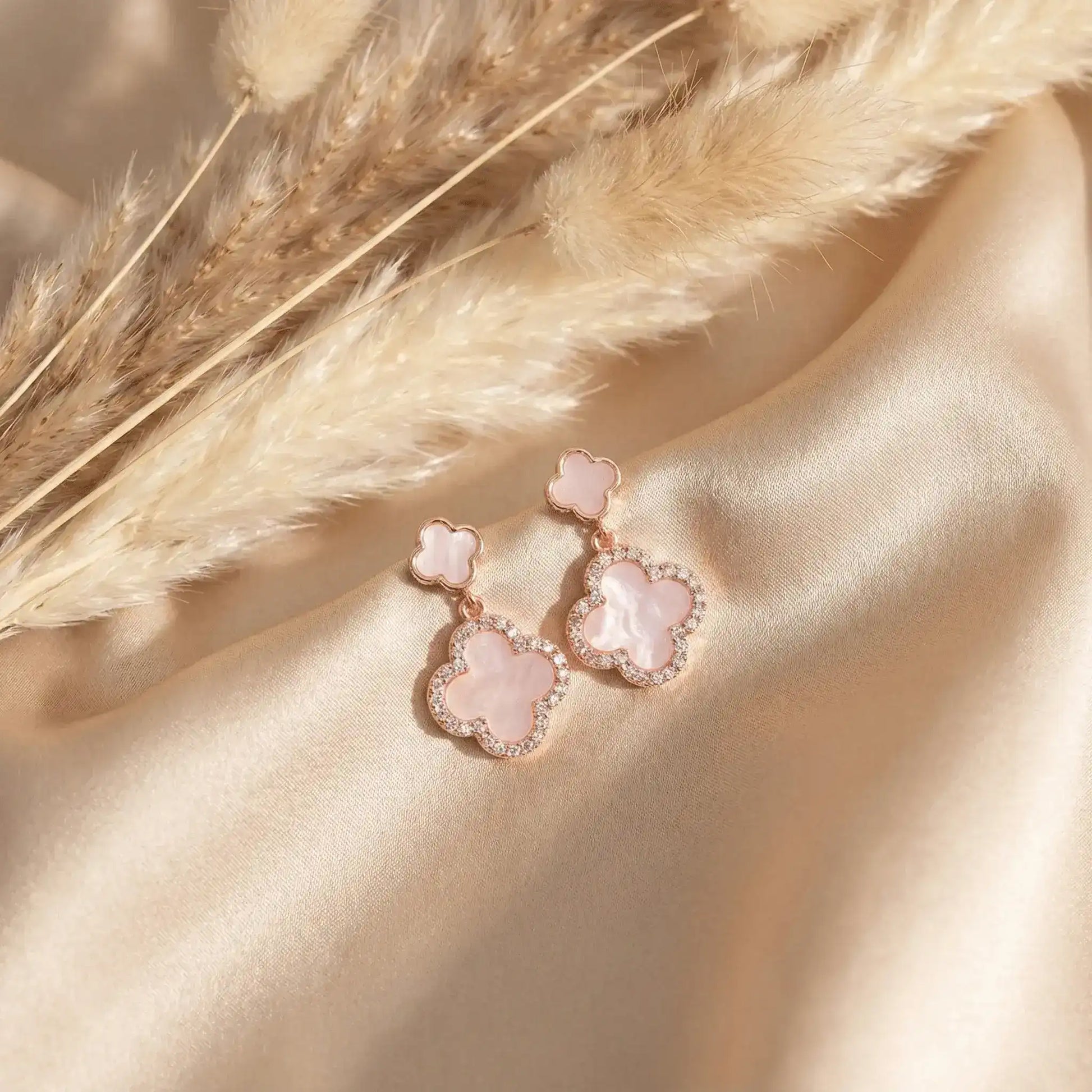 Rose gold clover drop earrings on beige satin with pampas grass