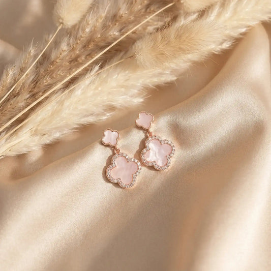 Rose gold clover drop earrings on beige satin with pampas grass