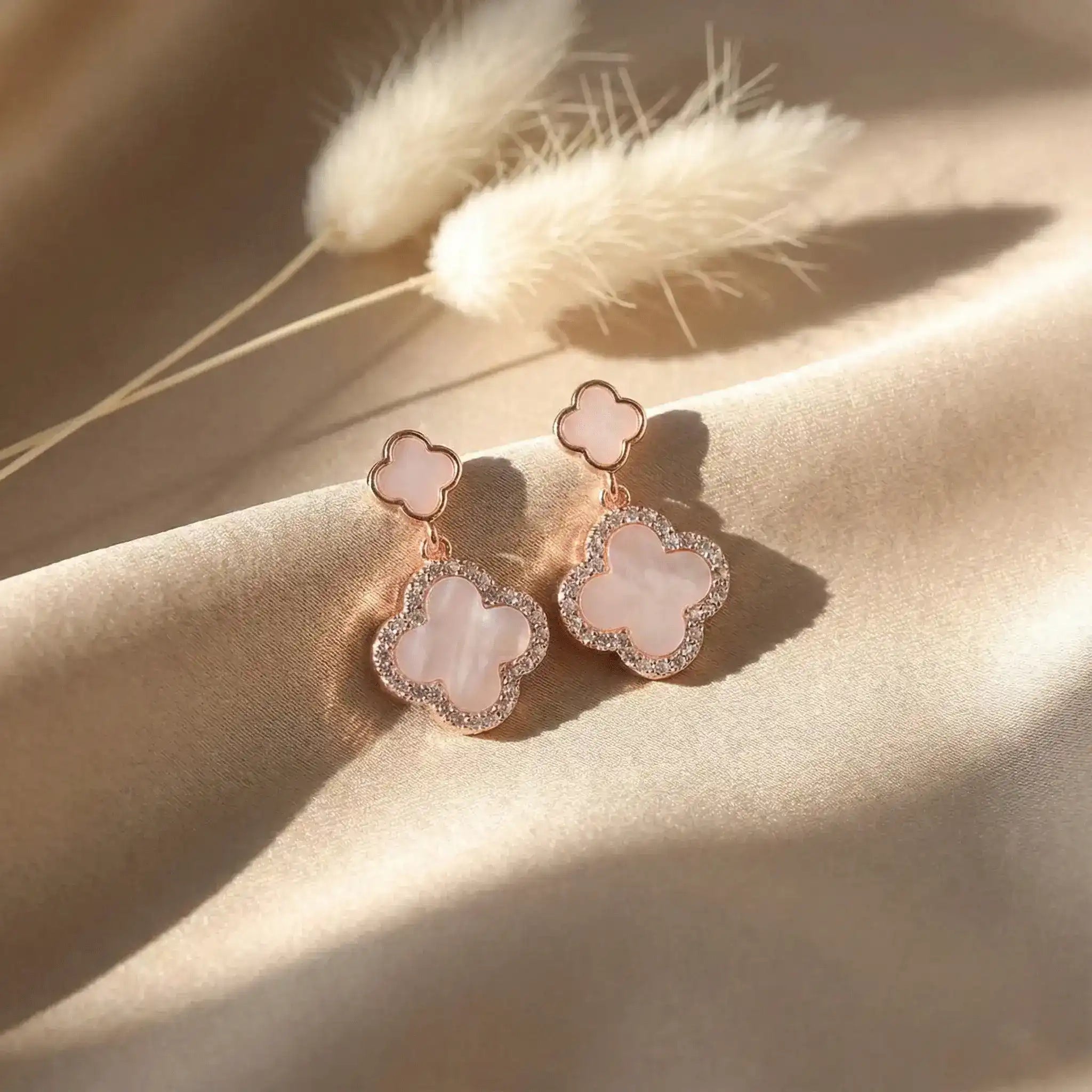 Rose gold clover drop earrings on beige satin with pampas grass