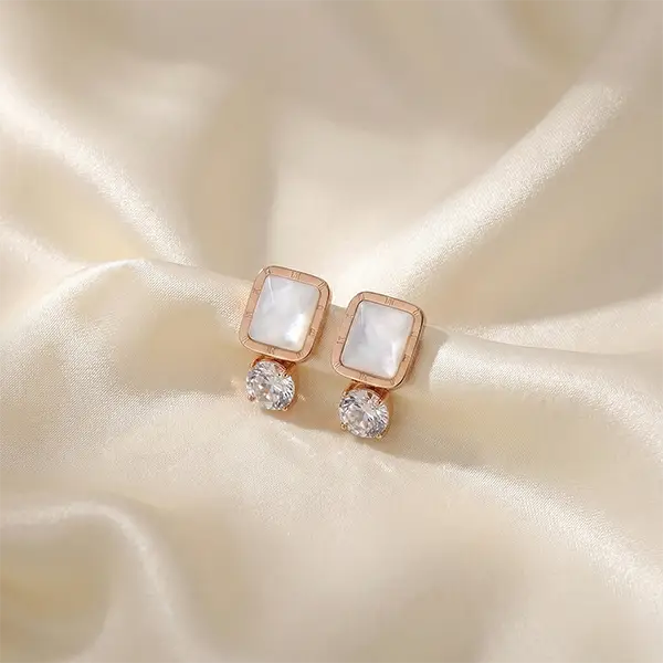 Rose gold square stud earrings with white stone and crystal drop placed on soft satin fabric