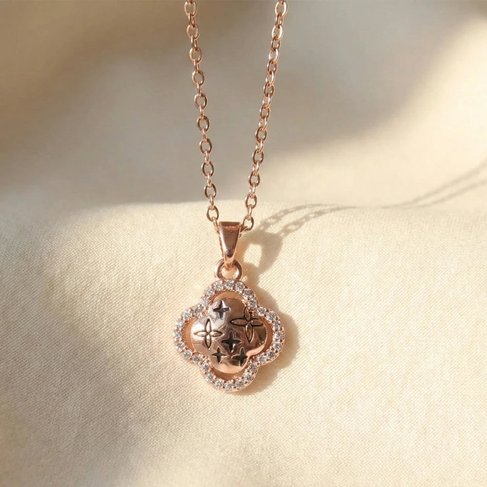 Rose gold clover pendant necklace with star engravings and a crystal-studded border displayed on soft cream fabric.