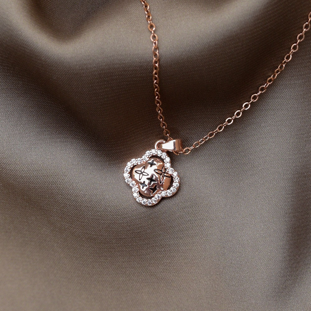 Rose gold clover pendant necklace with star engravings and a crystal-studded border displayed on brown satin cloth.