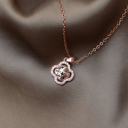 Rose gold clover pendant necklace with star engravings and a crystal-studded border displayed on brown satin cloth.