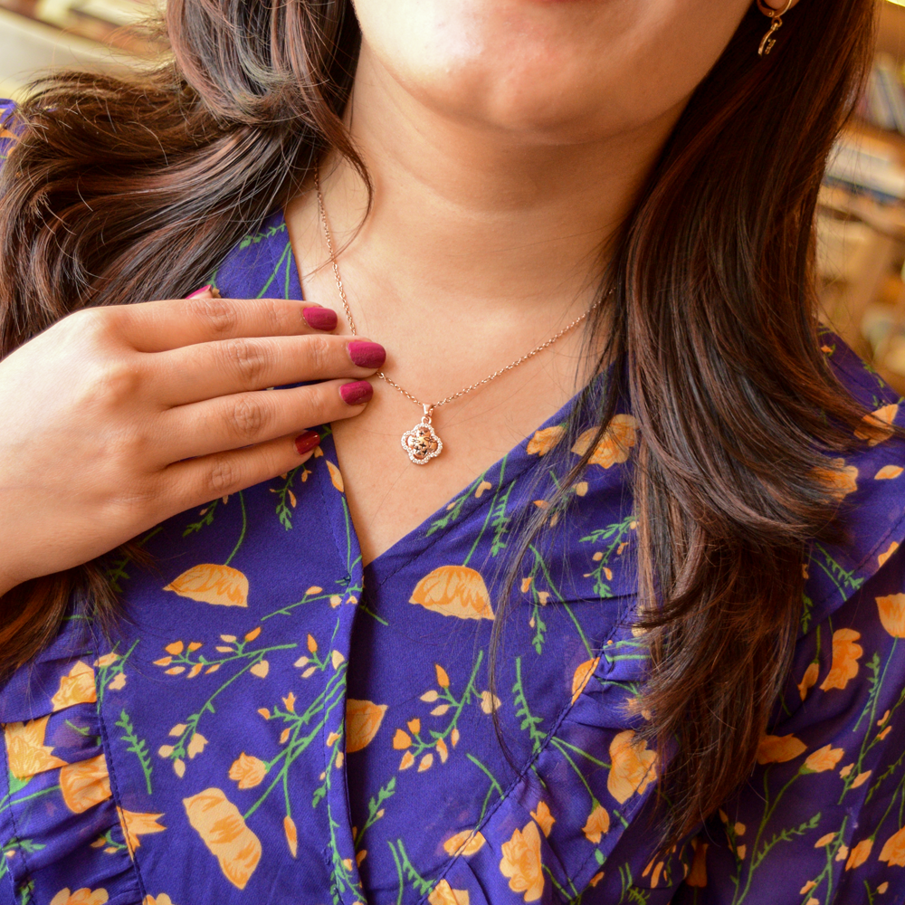 Rose gold clover pendant necklace with star engravings and a crystal-studded border displayed on a model.