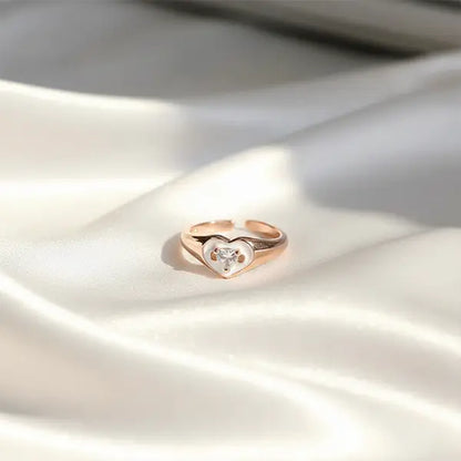 Rose gold heart-shaped ring with a sparkling crystal centerpiece displayed on soft satin fabric.