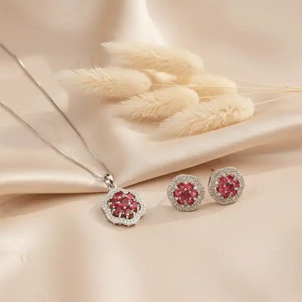 Ruby Bloom Necklace Set displayed on beige satin cloth with pampas grass, ruby pendant and earrings