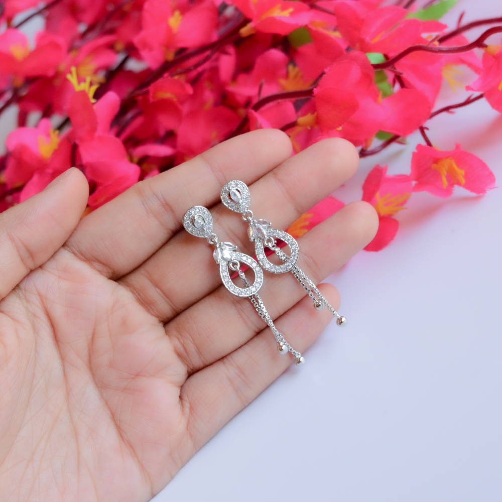 Shiny AD Danglers held in a hand with pink flowers in the background