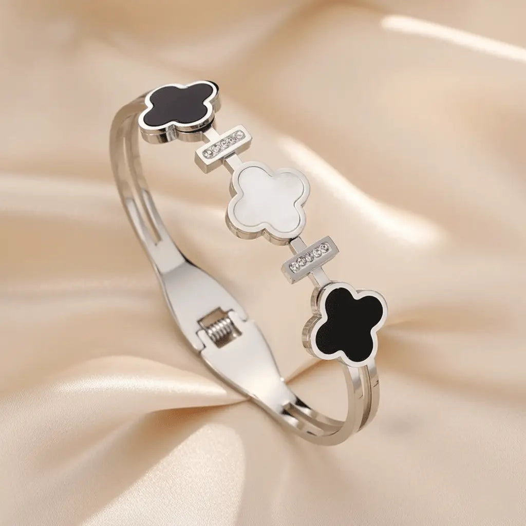Silver Clover Bracelet showcasing black and white clover designs and crystal bars placed on soft satin fabric.