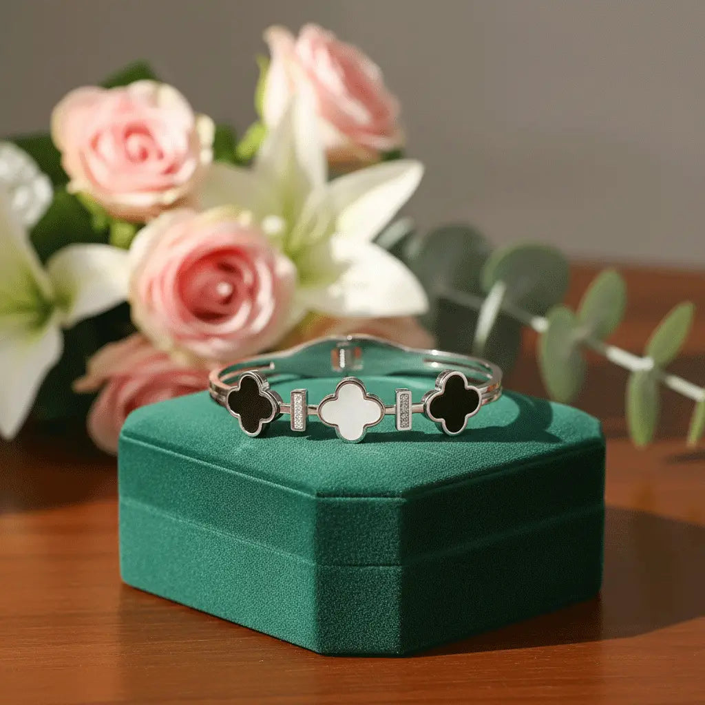 Silver Clover Bracelet with black and white clover charms displayed on a green velvet box with roses in the background.