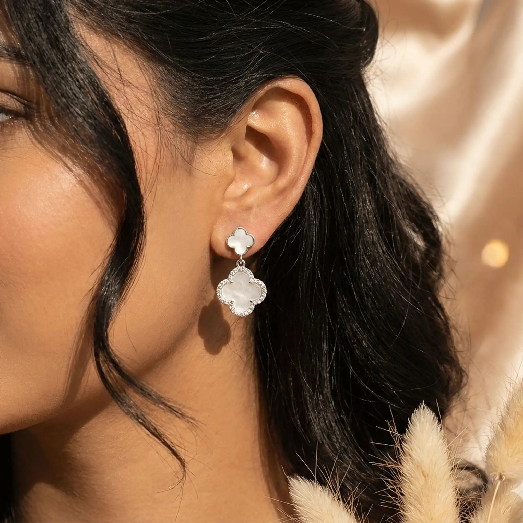 Silver clover drop earrings worn on ear in natural sunlight