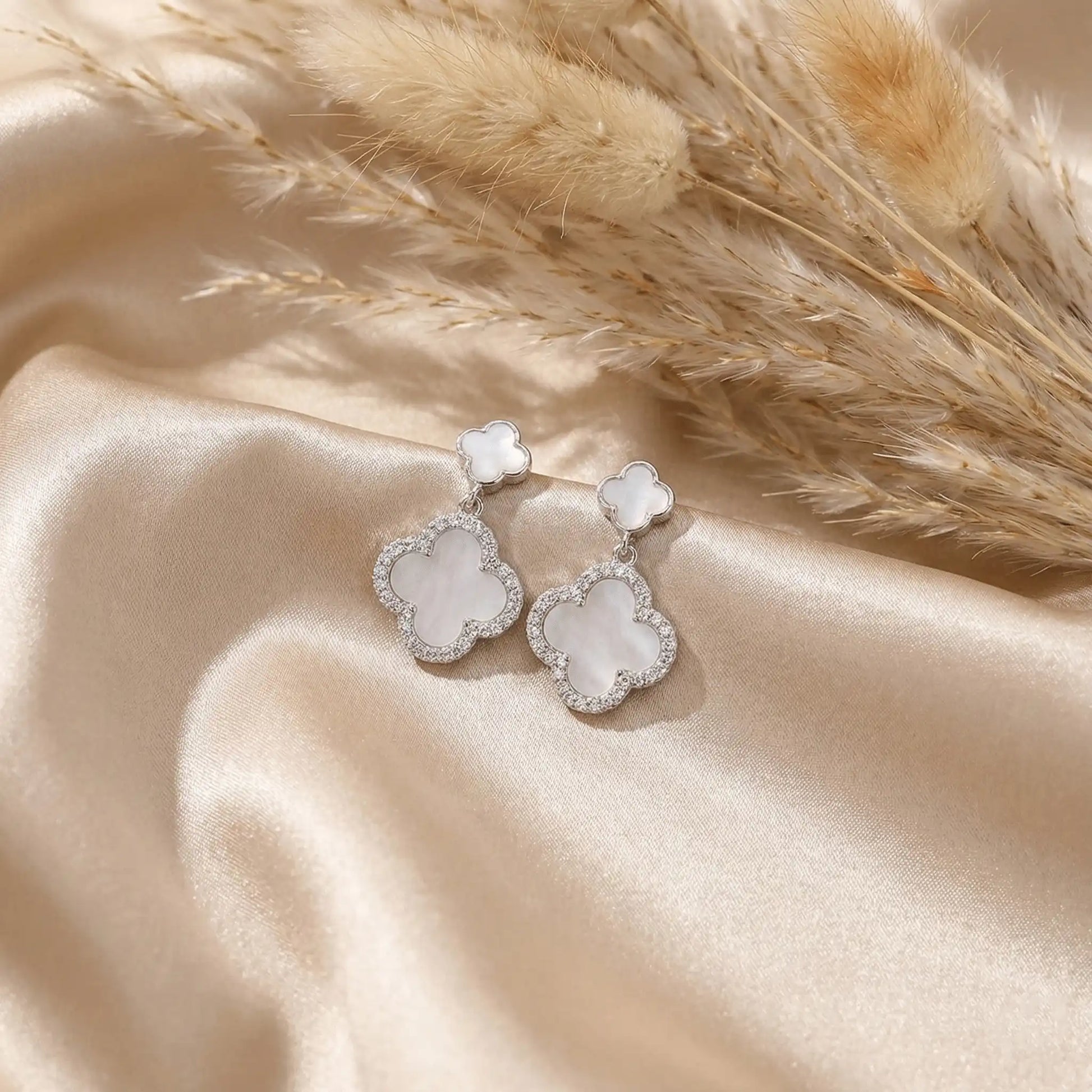 Silver clover drop earrings on satin fabric with pampas grass