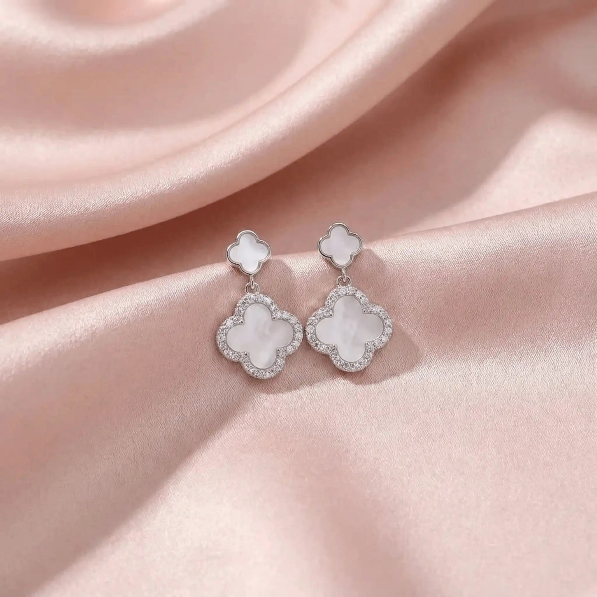 Silver clover drop earrings on blush pink satin background