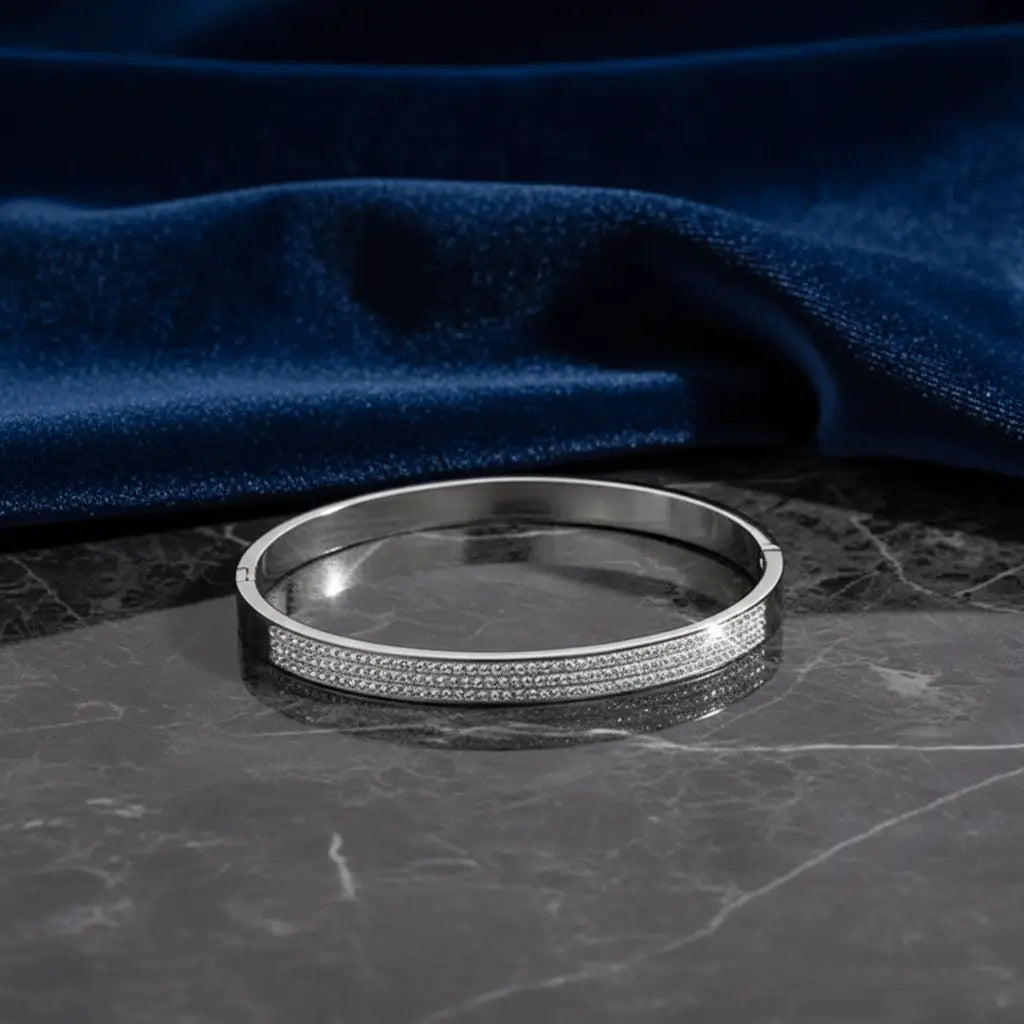 Stylish silver bangle bracelet with sparkling crystal detailing placed on dark marble with navy velvet fabric.