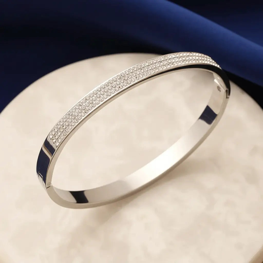 Shiny silver bangle bracelet with dense micro-pave crystal design showcased on a marble pedestal.