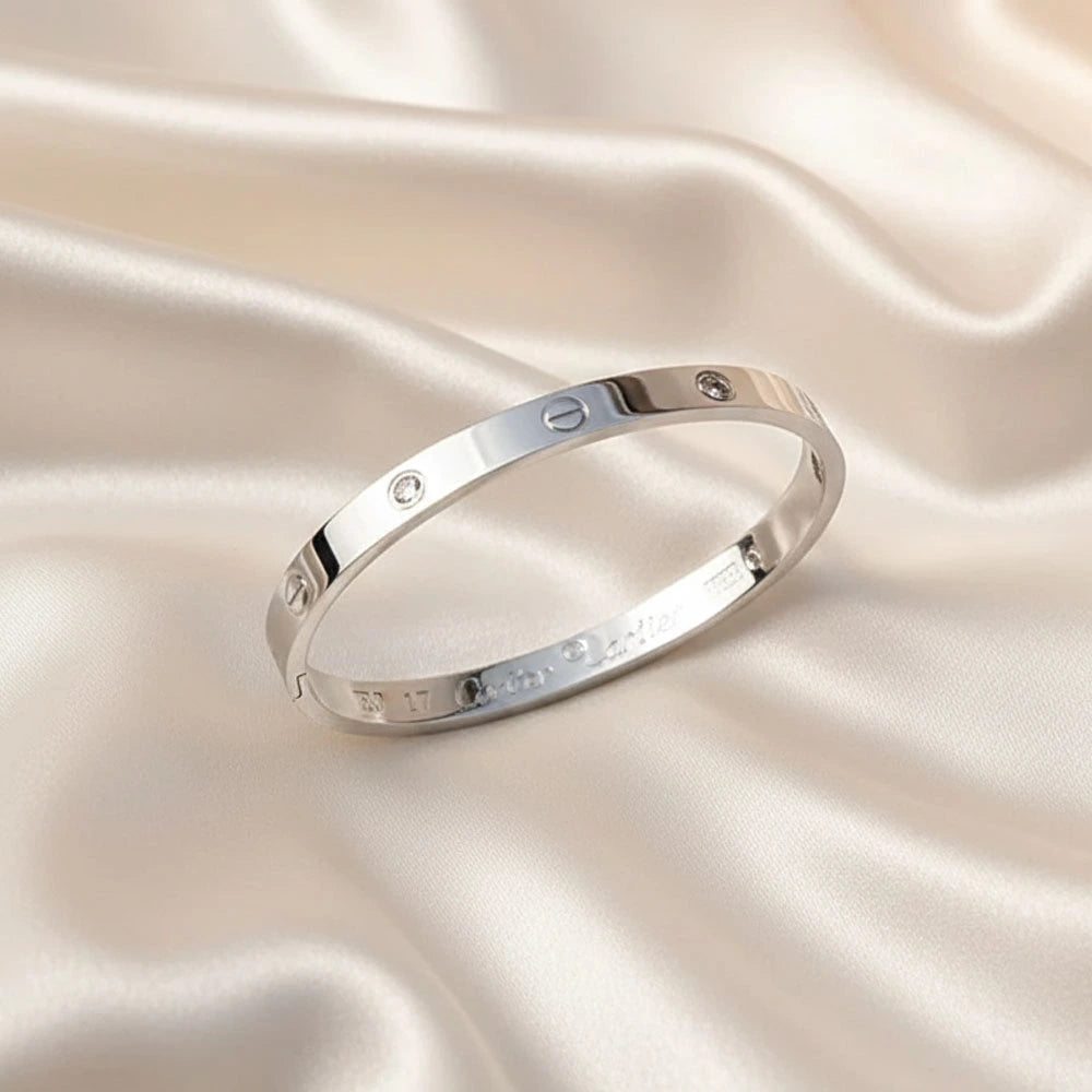 Silver cartier bracelet on a soft, light pink satin background.