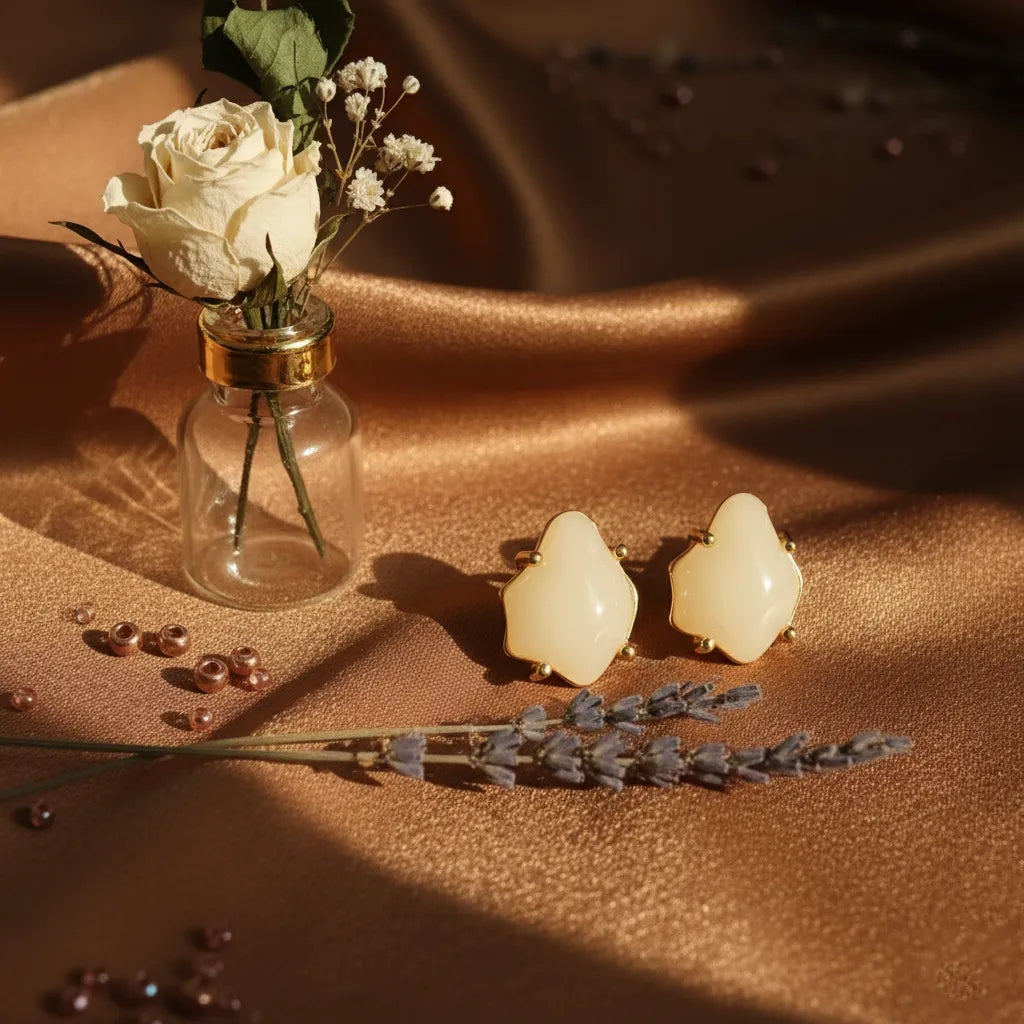 Soft Glow Studs by Ka Trends displayed on golden satin fabric beside a dried white rose in a glass bottle and lavender stems — aesthetic jewellery flatlay.