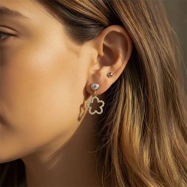 Woman wearing Starlit Clover Dangles in golden finish, featuring a crystal stud and clover-shaped drop design.