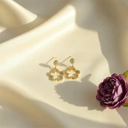 Starlit Clover Dangles in golden colour with crystal stud and clover drop displayed on soft cream satin with floral styling.