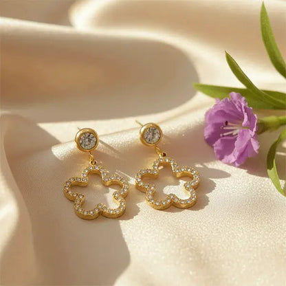 Golden Starlit Clover Dangles with crystal-studded clover design showcased on satin fabric beside a purple flower.