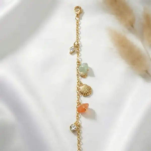 Close-up of gold charm bracelet featuring shell and gemstone charms, anti-tarnish finish