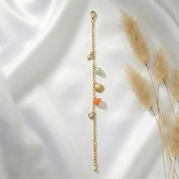 Flat lay of gold anti-tarnish charm bracelet with stones and shell details on soft fabric