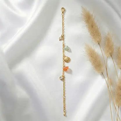 Flat lay of gold anti-tarnish charm bracelet with stones and shell details on soft fabric