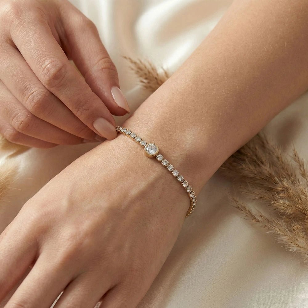 Gold stone tennis bracelet worn on a wrist, featuring a delicate central round stone and adjustable clasp.