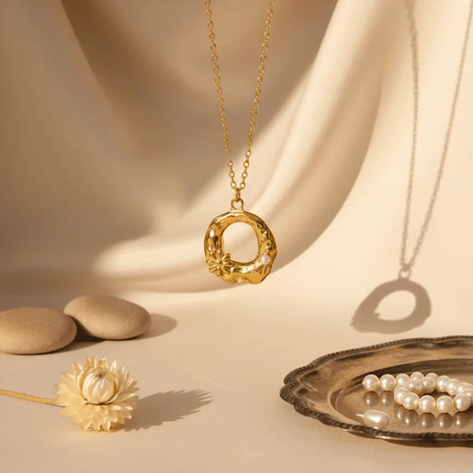 Textured round gold pendant necklace with floral detailing and pearls displayed on beige fabric with soft natural light.