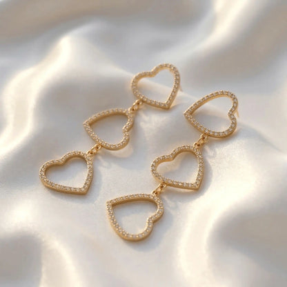 Three-Tier Heart Earrings with cascading open-heart designs and shimmering accents, resting on silky white fabric with gentle folds and highlights.