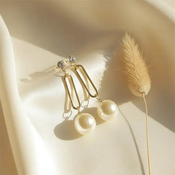 Timeless Pearl Drops earrings on beige satin cloth under warm natural sunlight with dried phalaris grass prop