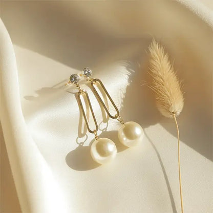 Timeless Pearl Drops earrings on beige satin cloth under warm natural sunlight with dried phalaris grass prop
