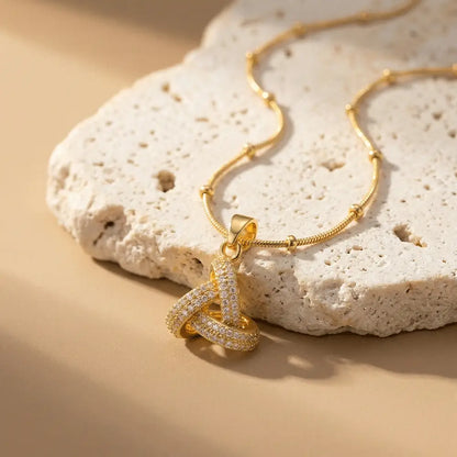 Minimal gold crystal knot pendant necklace on beige stone slab, anti-tarnish aesthetic jewelry by Ka Trends