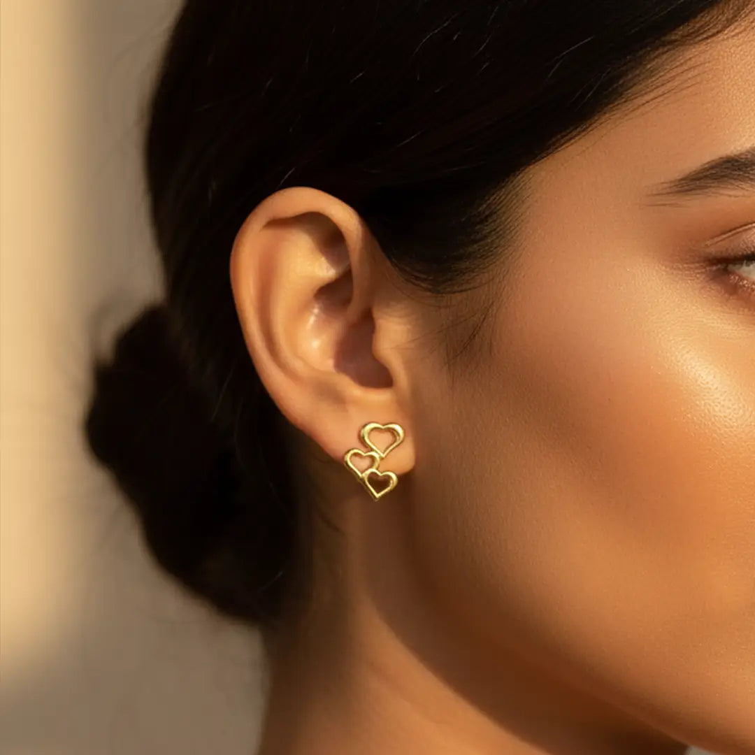 Triple Heart Drops gold earrings worn by an Indian woman in warm natural sunlight, close-up ear shot.