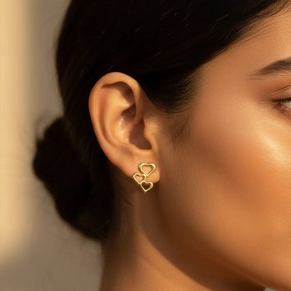 Triple Heart Drops gold earrings worn by an Indian woman in warm natural sunlight, close-up ear shot.