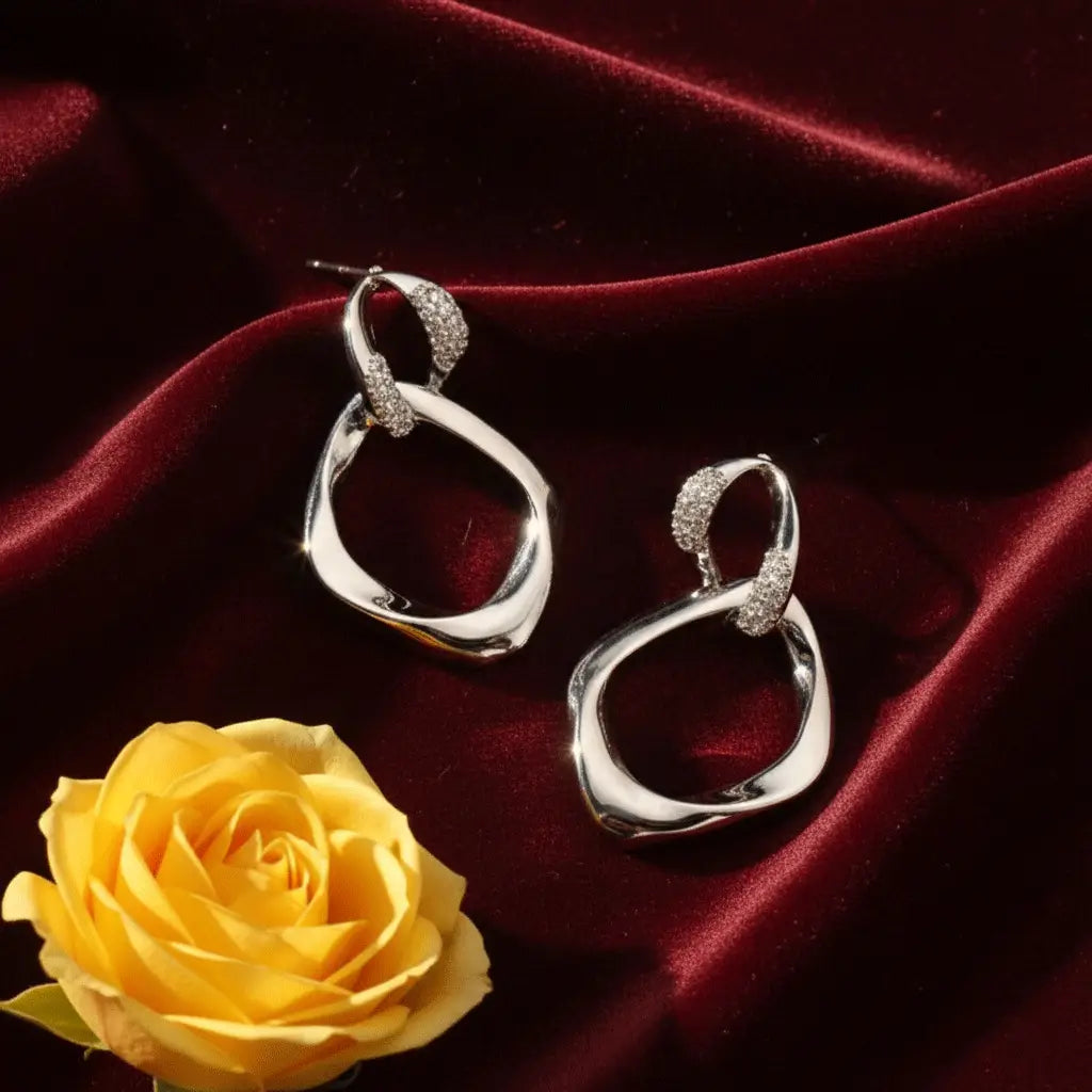 silver abstract drop earrings with crystal-studded loops displayed on deep red velvet with a yellow rose.