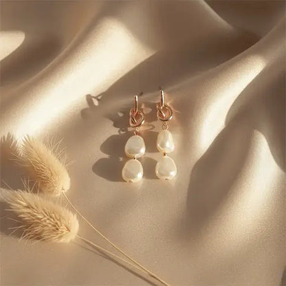 Elegant rose gold double pearl earrings on beige satin cloth with warm sunlight and dried phalaris grass props
