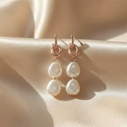 Close-up of rose gold double pearl dangle earrings on beige satin fabric under soft natural sunlight