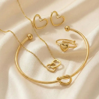 Valentine Special anti-tarnish heart jewellery combo with gold-tone heart earrings, adjustable bracelet, heart ring, and double-heart pendant necklace styled on a soft satin fabric background.