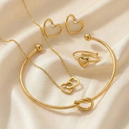 Valentine Special anti-tarnish heart jewellery combo with gold-tone heart earrings, adjustable bracelet, heart ring, and double-heart pendant necklace styled on a soft satin fabric background.