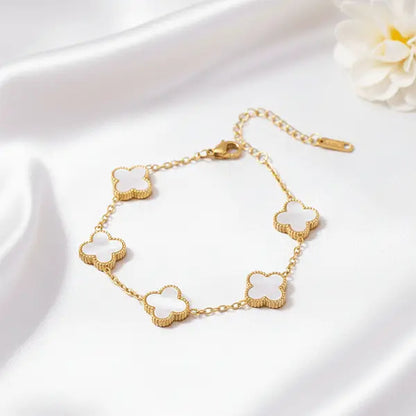 White Clover Bracelet featuring white clover charms in gold tone, displayed on white satin fabric with soft lighting
